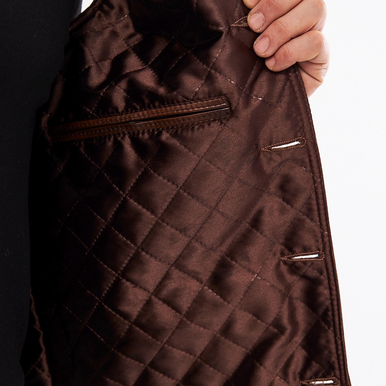 May include: A dark brown jacket interior featuring a quilted satin lining with a diamond pattern. The garment includes a horizontal welt pocket on the left side and a vertical row of buttonholes along the front edge, showcasing the construction.