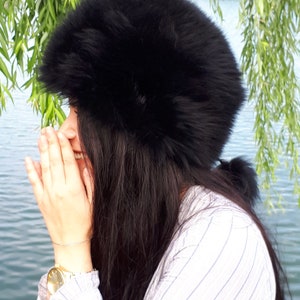 Peut inclure: Un chapeau en fausse fourrure noire, volumineux et arrondi, dot&eacute; d'une bande &eacute;paisse et textur&eacute;e. Le chapeau pr&eacute;sente un poil dense et doux qui recouvre toute la surface ext&eacute;rieure, offrant une silhouette pleine et arrondie sur la t&ecirc;te.