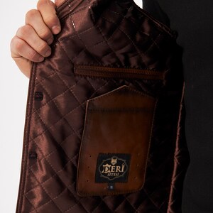 May include: A brown jacket interior featuring a quilted satin lining with a diamond pattern. The garment includes a brown leather interior pocket with a black rectangular label displaying the text DERI SITESI and a small graphic of a wolf head.