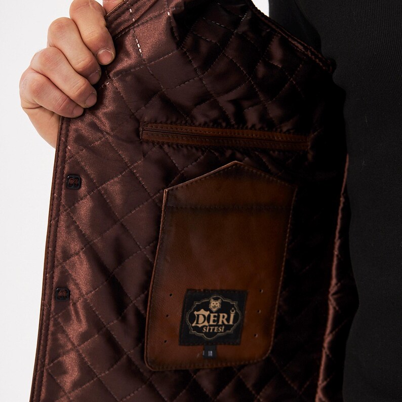 May include: A brown jacket interior featuring a quilted satin lining with a diamond pattern. The garment includes a brown leather interior pocket with a black rectangular label displaying the text DERI SITESI and a small graphic of a wolf head.