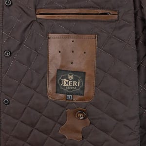 May include: A dark brown quilted jacket interior featuring a horizontal zippered pocket and a tan leather patch pocket. The patch pocket displays a black label with the text DERI SITESI and a size S tag. A spare button is attached to a leather swatch.