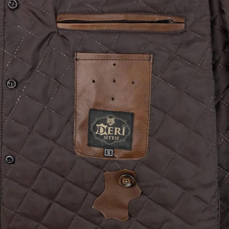 May include: A dark brown quilted jacket interior featuring a horizontal zippered pocket and a tan leather patch pocket. The patch pocket displays a black label with the text DERI SITESI and a size S tag. A spare button is attached to a leather swatch.