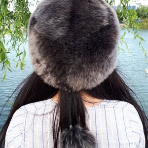 Peut inclure: Un chapeau rond en fausse fourrure gris fonc&eacute; avec une texture &eacute;paisse et pelucheuse. Le chapeau pr&eacute;sente un cordon de serrage noir suspendu &agrave; l'arri&egrave;re, termin&eacute; par un pompon en fausse fourrure gris fonc&eacute; assorti pour un d&eacute;tail d&eacute;coratif.