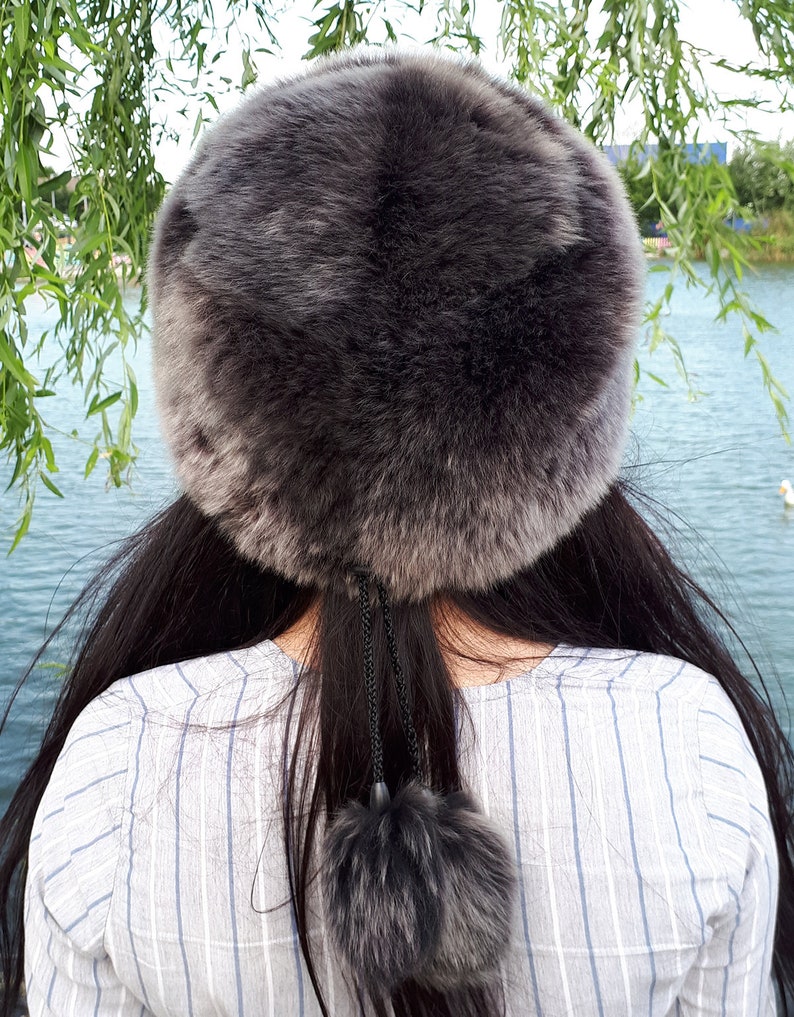 Peut inclure: Un chapeau rond en fausse fourrure gris fonc&eacute; avec une texture &eacute;paisse et pelucheuse. Le chapeau pr&eacute;sente un cordon de serrage noir suspendu &agrave; l'arri&egrave;re, termin&eacute; par un pompon en fausse fourrure gris fonc&eacute; assorti pour un d&eacute;tail d&eacute;coratif.