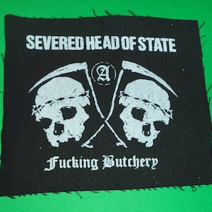 Può includere: Toppa quadrata nera con testo e grafica bianchi. Il testo recita "SEVERED HEAD OF STATE" e "Fucking Butchery". Due teschi con falci incrociate sono al centro. Sfondo verde.