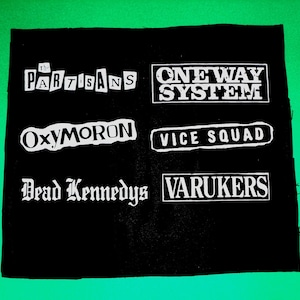 Peut inclure: Patch en tissu noir avec du texte blanc. Le texte indique "The Partisans", "One Way System", "Oxymoron", "Vice Squad", "Dead Kennedys", et "Varukers".