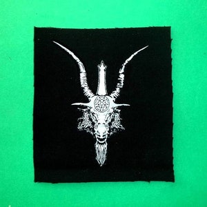 Op de afbeelding: Witte geborduurde patch op zwarte stof met een geitenkop met hoorns en een pentagram.