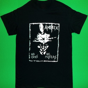 Pode incluir: Camiseta preta com uma estampa branca de um rosto com cabelo espetado e o texto "AMERIX NO GODS NO MASTERS".