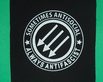 May include: Black and white patch with a circle containing three white arrows pointing to the left. The circle has the text "Sometimes Antisocial Always Anti-Fascist" around it.