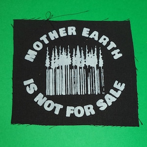 Pode incluir: Patch de tecido preto com texto branco que diz "Mother Earth is not for sale". Uma imagem estilizada de uma floresta está no centro do patch.