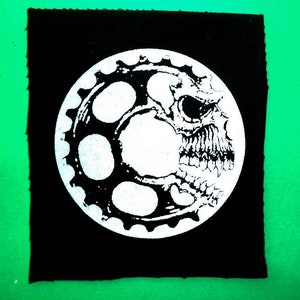 Peut inclure: Patch brodé noir et blanc représentant un crâne avec un motif d'engrenage. Le crâne est délimité en blanc et l'engrenage est rempli de blanc.