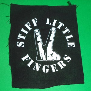 Könnte beinhalten: Schwarz-weiß-Patch mit dem Text "Stiff Little Fingers" in einem Kreis um ein weißes Peace-Zeichen.
