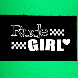 May include: Black patch with white text that reads "Rude***GIRL" with a checkered pattern and a heart.