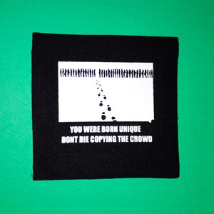 May include: Black and white patch with a graphic of a line of people walking away from a single set of footprints. The text reads "You were born unique. Don't die copying the crowd."