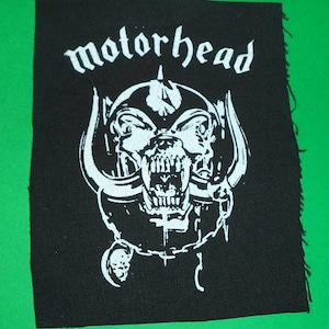 Könnte beinhalten: Schwarz-weiß gestickter Patch mit dem Bandnamen "Motorhead" und einem knurrenden, gehörnten Schädel-Motiv.