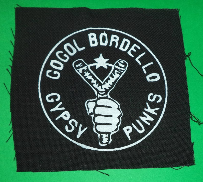 May include: Black and white embroidered patch with a circle design. The circle features a slingshot with a star above it and the text "Gogol Bordello Gypsy Punks".