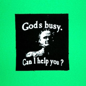 May include: Black and white patch with a graphic of a spiky-haired person and the text "God's busy. Can I help you?"