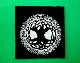 May include: Black and white embroidered patch with a tree of life design on a black fabric background.