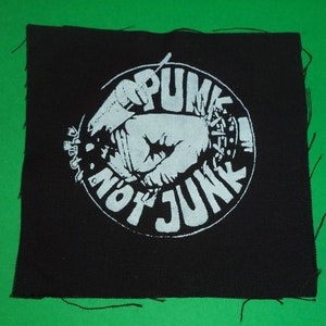 Può includere: Toppa in tessuto nero con un cerchio bianco che contiene un pugno che tiene un microfono e il testo "Punk Not Junk".
