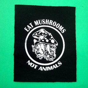 Könnte beinhalten: Schwarz-weißes Bügeleisen-Patch mit dem Text "Eat Mushrooms Not Animals" in einem Kreis mit einer Zeichnung von Pilzen darin.