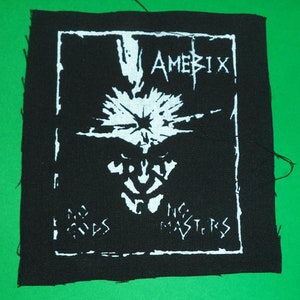 Peut inclure: Patch brodé noir et blanc avec le texte "Amebix" et "No Masters" dans une police gothique. Le patch présente un crâne stylisé avec un motif d'éclair.