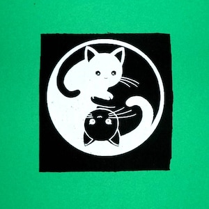 Op de afbeelding: Zwart-wit yin yang symbool met twee katten, een witte en een zwarte, die elkaar aankijken.