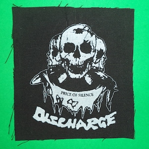 Peut inclure: Patch brodé noir et blanc avec un motif de crâne et d'os croisés. Le texte "Price of Silence" et "Discharge" est visible sur le patch.