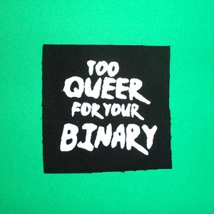 Peut inclure: Écusson en tissu noir avec du texte blanc qui dit "Too Queer For Your Binary".