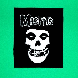 Könnte beinhalten: Schwarz-weißes Bügeleisen-Patch mit dem Bandnamen "Misfits" in weißem Text und einem weißen Totenkopf mit einem grinsenden Gebiss.