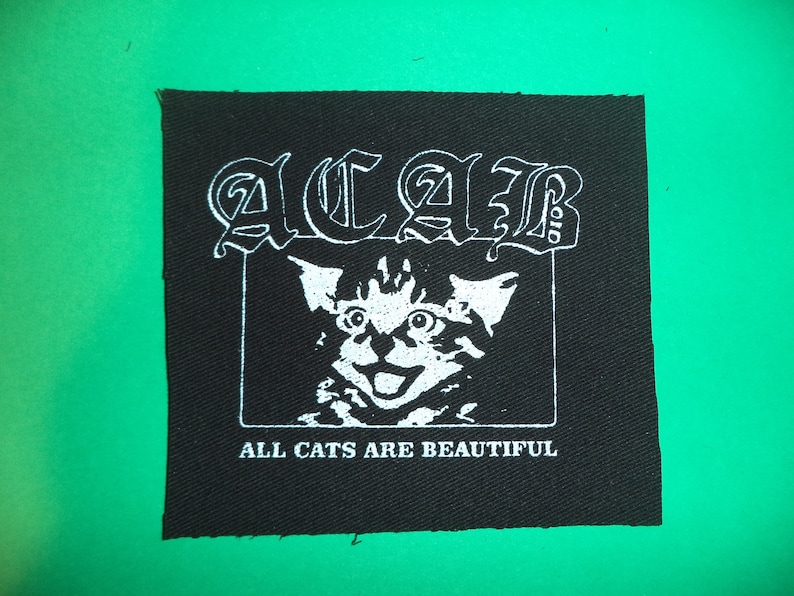 Op de afbeelding: Zwart-witte patch met een wit kattengezicht en de tekst "ACAB" boven de kitten en "ALL CATS ARE BEAUTIFUL" onder de kitten.
