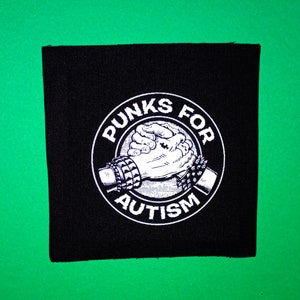 Könnte beinhalten: Schwarzer quadratischer Aufnäher mit den Worten "PUNKS FOR AUTISM" in einem weißen kreisförmigen Design. Das Design zeigt zwei Hände, die sich umfassen, eine mit einem Nietarmband und die andere mit einem Kreuztattoo. Der Aufnäher befindet sich auf grünem Hintergrund.