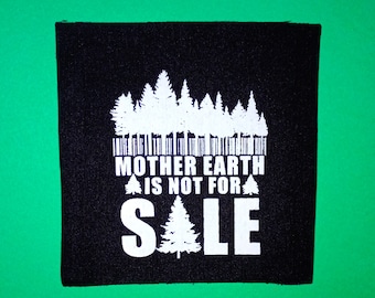 May include: A black square patch with white text and a forest graphic. The text reads "MOTHER EARTH IS NOT FOR SALE" with a stylized tree graphic. The patch is set against a green background.