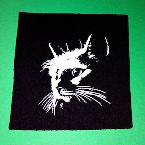 May include: A black and white iron-on patch featuring a close-up of a cat's face. The cat is looking to the right of the image.