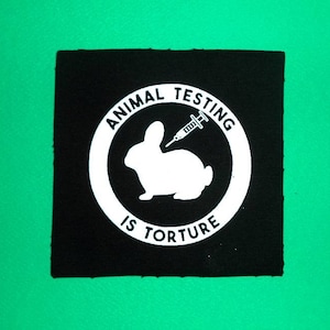 May include: Black and white patch with a circle containing a rabbit with a needle in its back. The text "ANIMAL TESTING IS TORTURE" is written around the circle.