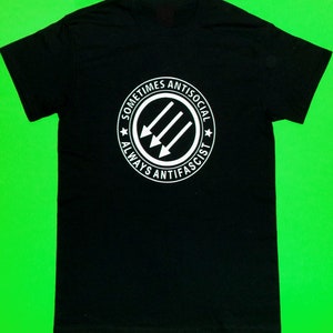 May include: Black t-shirt with a white circle graphic that says "Sometimes Antisocial Always Anti-Fascist" with three arrows pointing to the right.
