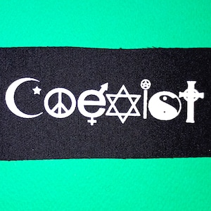 May include: Black fabric patch with the word "coexist" written in white. The word is made up of various religious symbols including a crescent moon, a peace sign, a yin yang, a Star of David, a cross, and a symbol for the female gender.