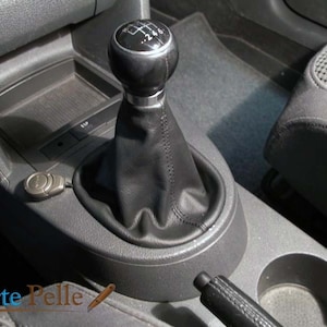 Può includere: Primo piano di un soffietto del cambio in pelle nera con una leva del cambio argentata. La leva ha i numeri 1, 2, 4, 5 e 6. Il cambio è all'interno di un'auto.