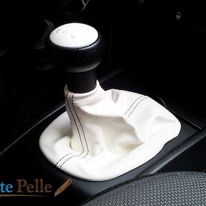 Puede incluir: Funda de palanca de cambios de cuero blanco con costuras negras. La funda está instalada en la palanca de cambios de un coche. La imagen incluye el texto "l'Arte Pelle".
