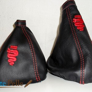 Peut inclure: Deux soufflets de levier de vitesse en cuir noir avec des coutures rouges et un logo Alfa Romeo brodé en rouge.