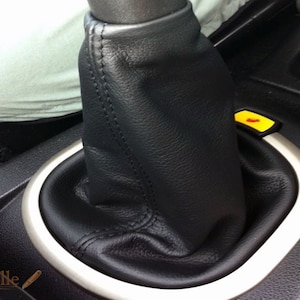 Può includere: Fodera per leva del cambio in pelle nera con cuciture. La fodera è installata nella console centrale di un'auto.