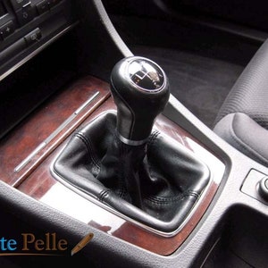 May include: Close-up of a black leather car gear shifter with a silver knob and a chrome trim. The shifter is surrounded by a wood-grain console.