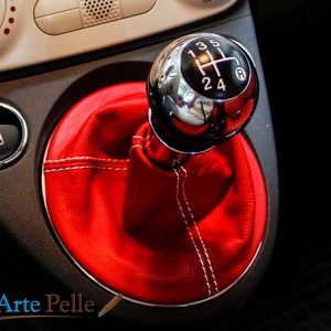 Puede incluir: Funda de palanca de cambios de cuero rojo con costuras blancas y pomo de palanca de cambios cromado con números negros 1, 3, 5, R, 2, 4.