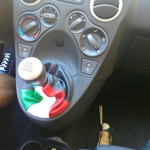 May include: A car's interior with a gear shift knob covered in a green, white, and red leather cover. The cover resembles the Italian flag. The knob has the numbers 1, 2, 3, 4, 5, and 6 on it. The car's dashboard has a variety of buttons and knobs.