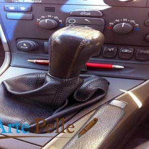 Könnte beinhalten: Schwarzer Lederschalthebelbalg mit Steppnähten für ein Auto. Der Balg ist in einem Auto mit beigefarbenem Innenraum verbaut.