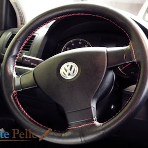 Puede incluir: Volante de cuero negro con costuras rojas. El volante presenta el logotipo de Volkswagen en el centro. La imagen muestra el volante y parte del salpicadero.