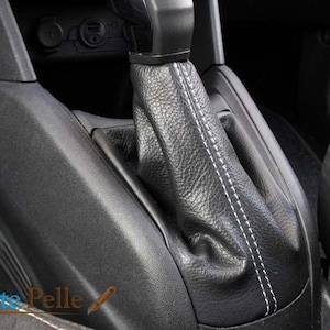 May include: Close-up of a black leather gear shift boot with white stitching. The boot is installed in a car's center console.