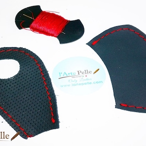 Puede incluir: Tres piezas de cuero negro con costuras rojas. Las piezas son para un proyecto de artesanía de cuero. Las piezas están cortadas en forma de lágrima, semicírculo y lágrima con un agujero en el centro. También se incluye un carrete de hilo rojo y una aguja.