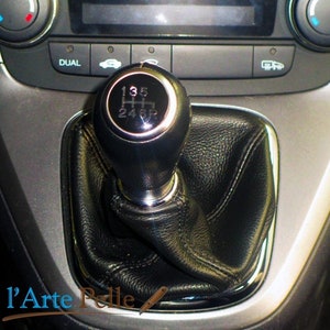 May include: Close-up of a black leather gear shift knob with a silver trim. The knob has a silver gear pattern with the numbers 1, 3, 5, R, 2, 4, and 6 printed on it.