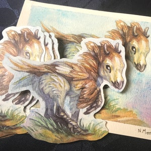 May include: A set of four watercolor stickers featuring a whimsical creature with brown fur, wings, and horns. The creature is depicted in a running pose with a light blue background.