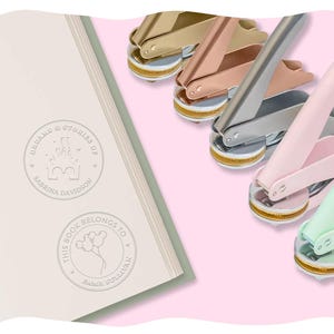 Puede incluir: Una colección de sellos de lacre en varios colores metálicos, incluyendo dorado, oro rosa y plateado, junto a un libro con texto en relieve. Las páginas del libro muestran las frases "DREAMS & STORIES OF" y "THIS BOOK BELONGS TO".